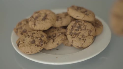 Colocación manual de galletas con chispas de chocolate en un plato blanco, ángulo alto