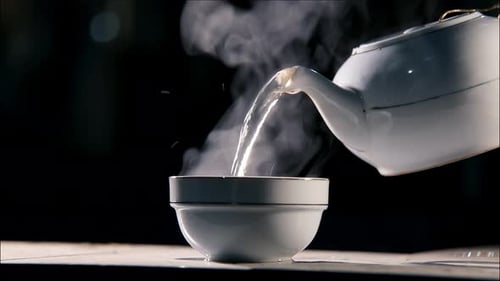 Cup napolnyaetsya zelenym chaem. Pouring a hot drink from a ceramic kettle and a cup.