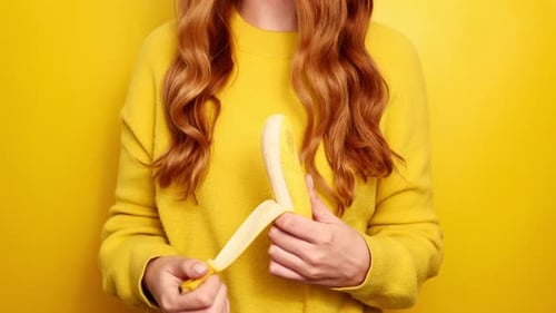 Redhead woman peeling banana at yellow background. Close up of young Caucasian lady enjoying healthf
