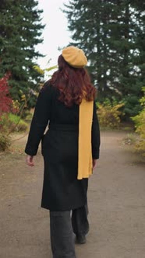 Back View of Young Woman Walking Through Vibrant Garden Wearing Yellow Beret and Scarf