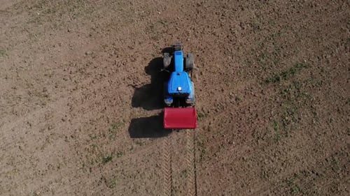 Blue Tractor Tilling Brown Field From Above