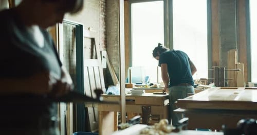 Two woodworkers skillfully crafting wood pieces inside bright workshop