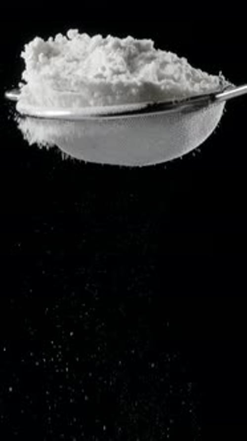 Sift icing sugar or powdered sugar or flour through a sieve tool on black background.