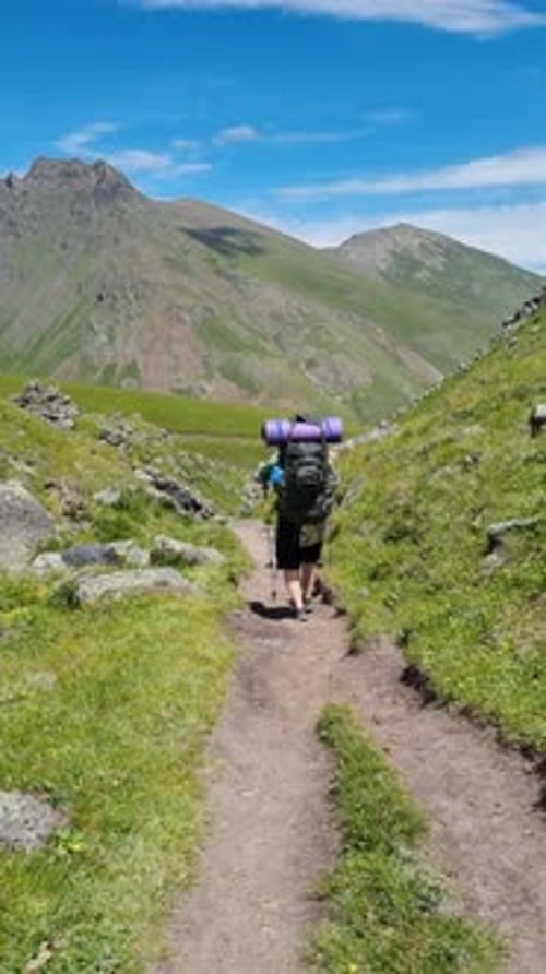 Vidéo verticale d'un randonneur marchant sur un sentier en montagne avec un sac à dos et des bâtons de randonnée