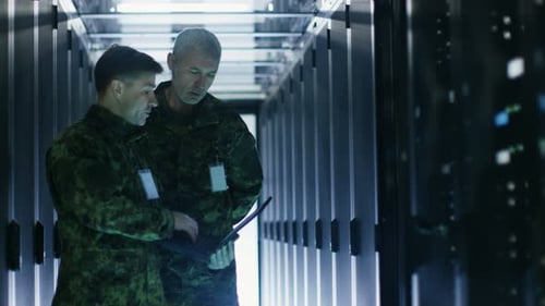 In Data Center Two Military Men Work with Open Server Rack Cabinet. One Holds Military Edition Lapt