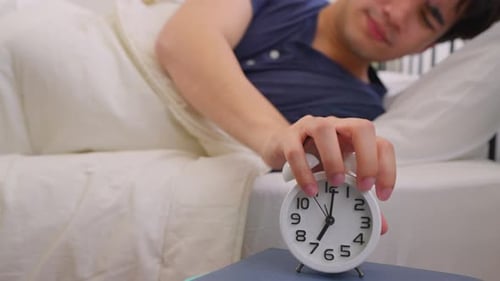 Asian attractive young man turn off alarm clock ringing in the morning.