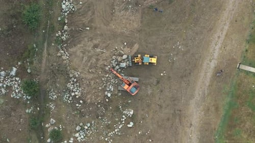 Aerial top-down view of two backhoes working and moving rocks at a construction site.