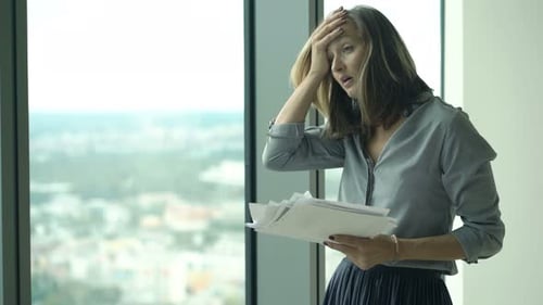 Upset, Sad Businesswoman Working with Documents by Window in Office 30s