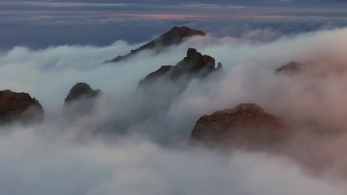 Serene Fog Envelops Towering Rocky Peaks with Warm Sunset Hues