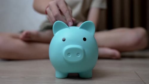 Saving Money in a Turquoise Piggy Bank by a Child at Home