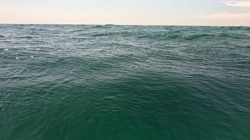 Sea Water Surface Camera Flies Over the Calm Azure Sea with Volcanic Rocky Shores on Background