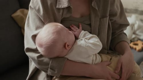 Mujer anónima sentada en el sofá acunando y amamantando al bebé