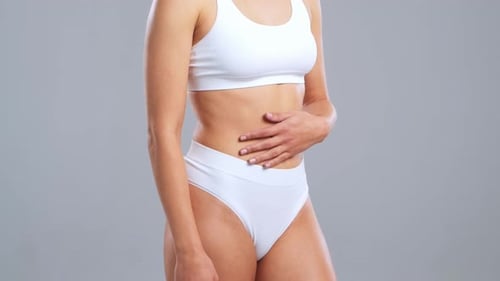 Jeune femme blonde en forme et belle en maillot de bain blanc posant sur fond gris Healthcare Diet