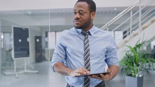 Handsome Young Black Manager in a Shirt Walking Pass His Business Colleagues with a Tablet and Supe