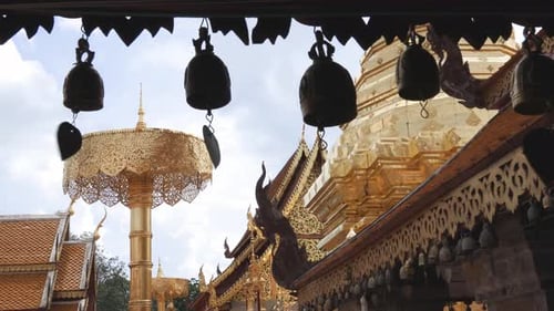 Row of small temple bells hanging from the eaves with background of gold plated chedi and buildings