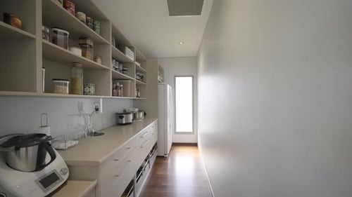 Contemporary modern kitchen. White stone top bench and white cabinetry. Large walk in pantry leading