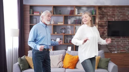 Happy cheerful senior married couple having fun at home. older family is dancing. Gray haired retire
