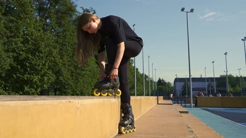 young beautiful girl in park tying laces on roller skates before skating workout active lifestyle
