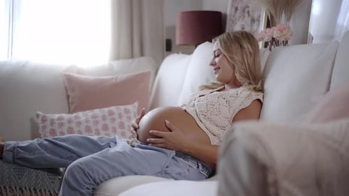 беременная женщина гладит живот, отдыхая на диване