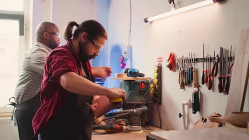 Woodworker Sands Wood in Workshop with Assistant