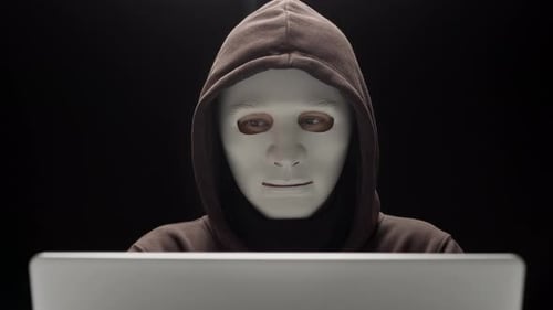 Anonymous Hooded Figure in Mask Using Laptop