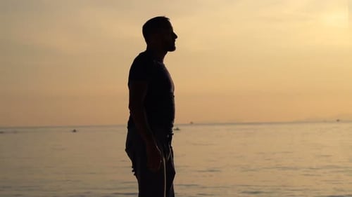 Silhouette of a young man walking on a tropical beach at sunset in super slow motion