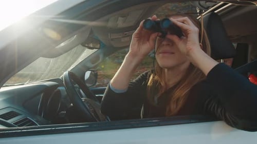 Woman Driving Car in Rural Area with Binoculars