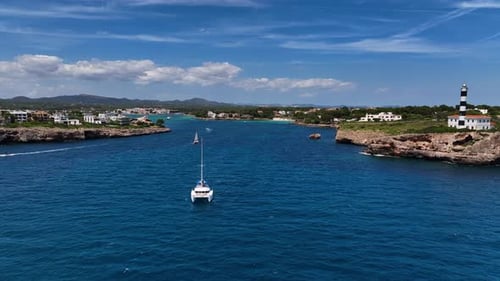 Beautiful Sailboats Drifting In A Deep Blue Bay With Lighthouse