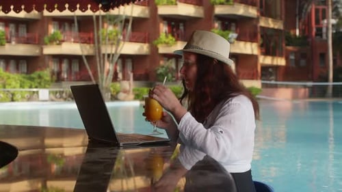 Woman Working on Laptop Sitting in Pool Drinking Cocktail in Bar on Vacation