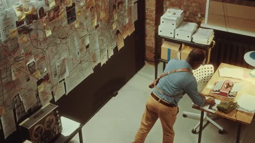 Black Detective Pinning Paper Note to Evidence Board in Dimly Lit Office