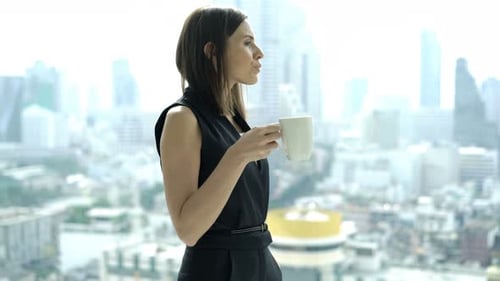 Young Businesswoman Drinking Coffee and Admire View From Window in Office 30s