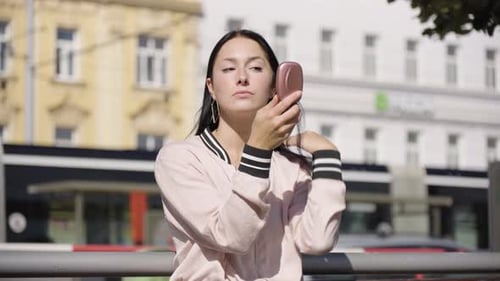 A Young Beautiful Caucasian Woman Checks Herself and Fixes Herself in a Mirror in an Urban Area
