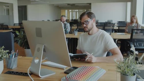 Businessman Using Computer and Taking Notes at Office Workplace