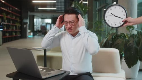 Chinese Businessman Working on Laptop with Anxiety Checking Time on Clock Deadline at Hotel Lobby