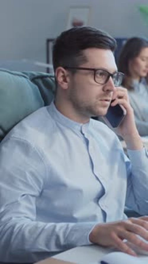 The Young Attractive Businessman is Talking on the Phone in the Office Using the Computer Working