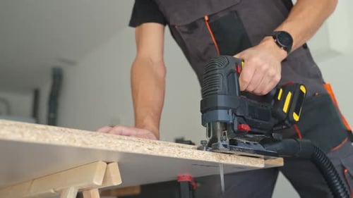 Man Cutting Chipboard with Electric Jigsaw in Home Garage Workshop
