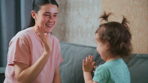Smiling Woman Plays with Little Girl on Couch