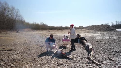 Family on picnic near the river with their dog roasting sausages