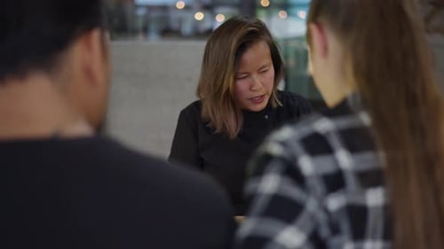 Woman Talking to Coworkers at Table Indoors