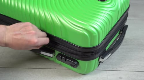 Guy opens and closes green baggage case with clothes in hand luggage zip up zipper. Man packing