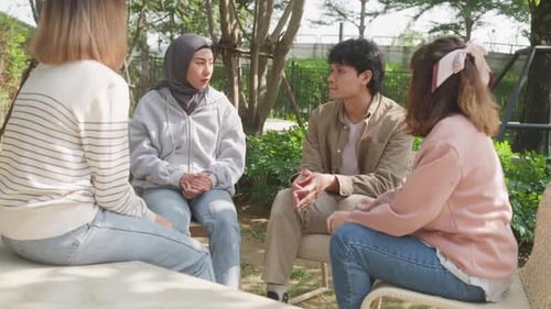 Small Asian group of people sit in a close circle and talk to a therapist in park.