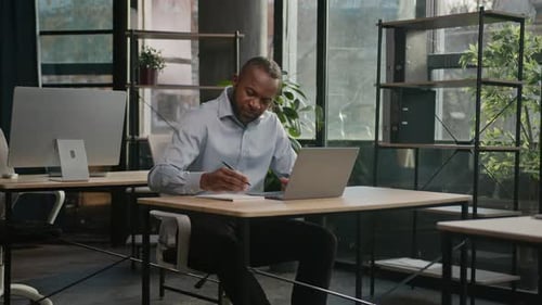 Man Works at Desk with Laptop in Bright Office