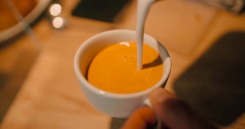 Close up hand of barista pouring latte art with espresso and milk froth in white hot ceramic cup