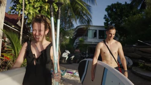 Couple Walking with Paddleboards on Tropical Beach