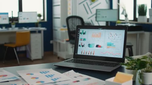 Closeup of Laptop Screen Showing Moving Charts and Financial Data in Empty Modern Office