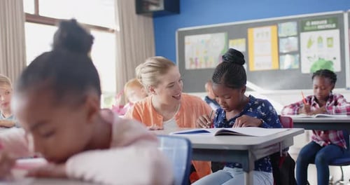 In school, female teacher helping student with writing assignment in classroom