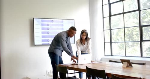 Discussing project details, colleagues using laptop and presentation screen in office