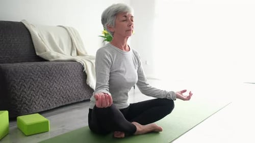 Active Senior Woman Practicing Yoga At Home Sitting In Lotus Pose