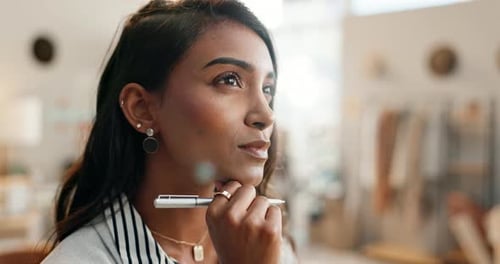 Business woman, face and thinking with pen in brainstorming, planning or strategy at office