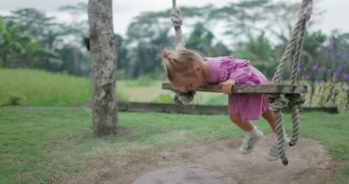 Little Child Girl Plays and Swinging on Wooden Swings Enjoy Childhood